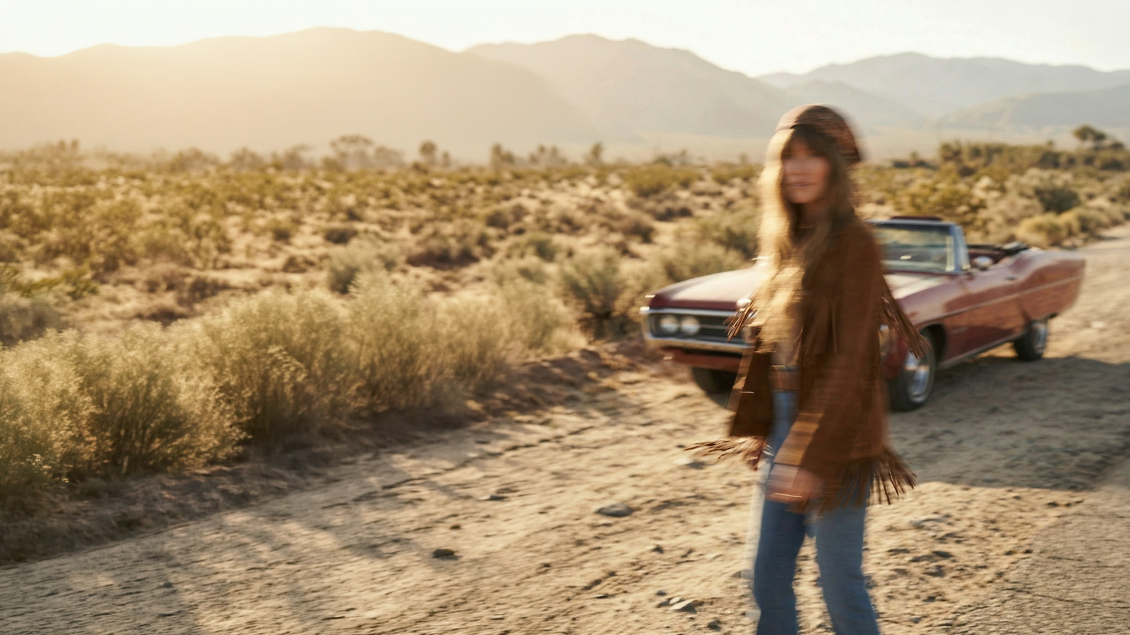 Woman standing in a desert with a vintage car in the background